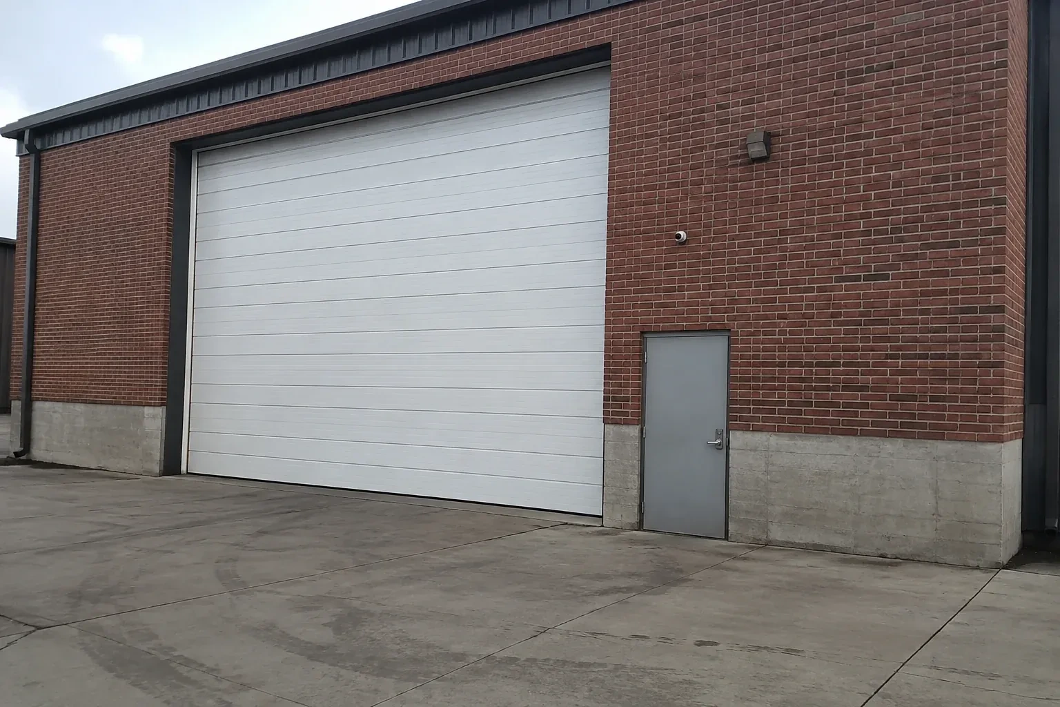 Tall closed sectional loading door beside a personnel door at a brick unit. — Commercial Sectional Door Repair, Woolwich