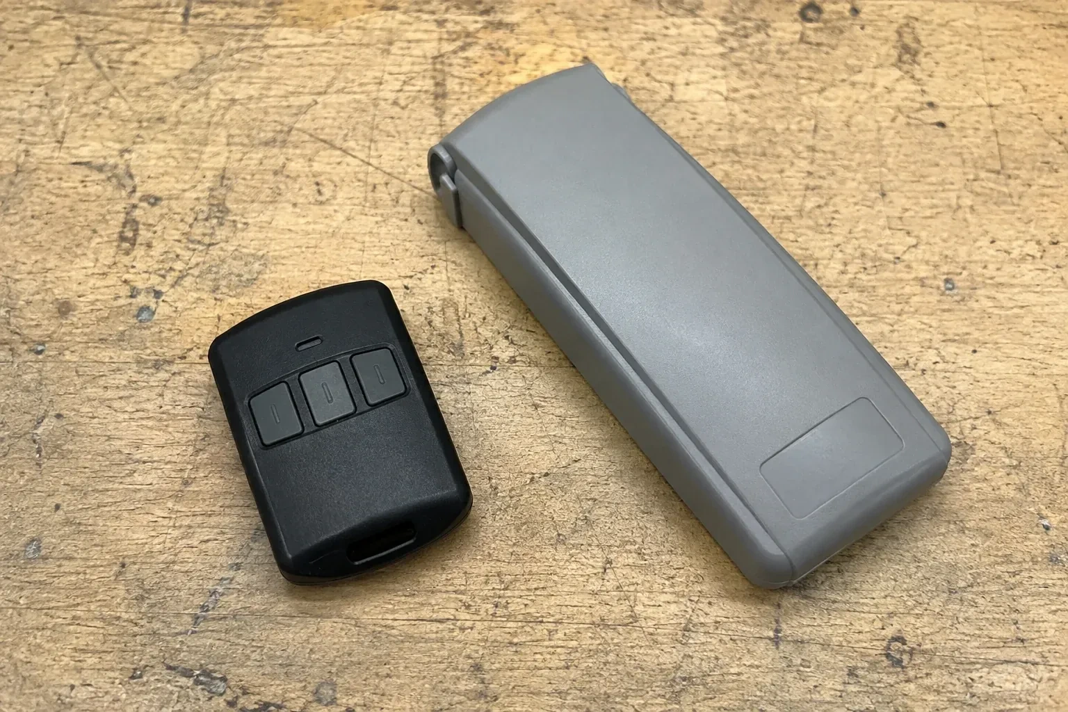 Three-button remote beside a closed grey keypad cover on a workbench. — Garage Door Remote and Keypad Programming, Woolwich