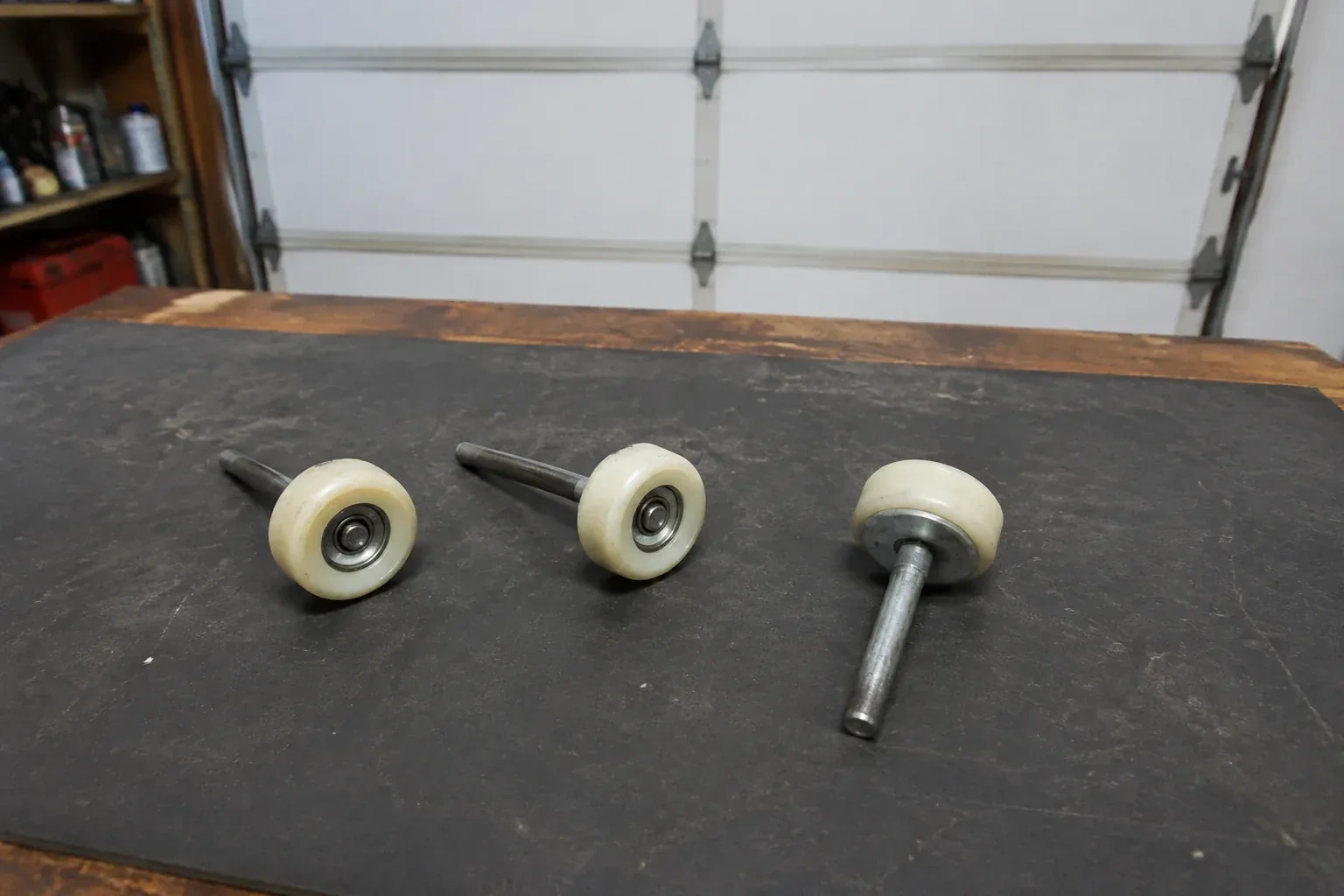 Three detached nylon-wheel garage door rollers with steel stems on a work mat. — Garage Door Roller Replacement, Woolwich